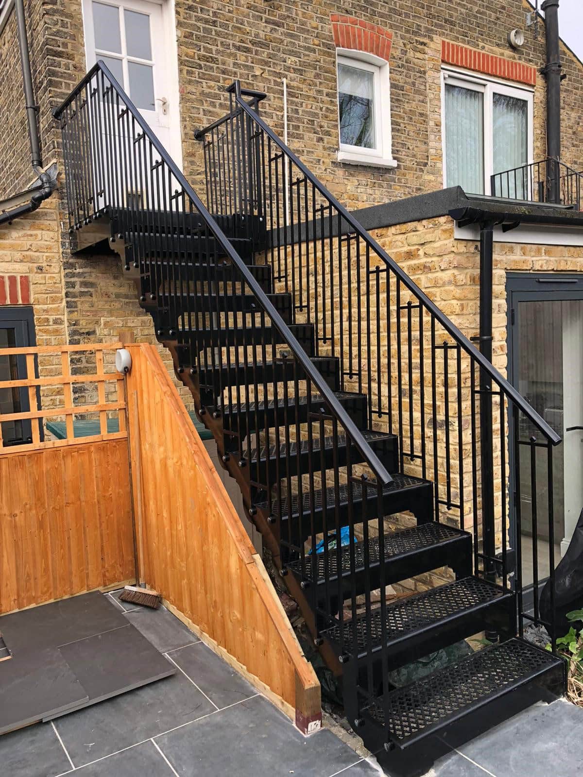 Outdoor metal staircase with black railing and steps, leading to a second-floor entrance.