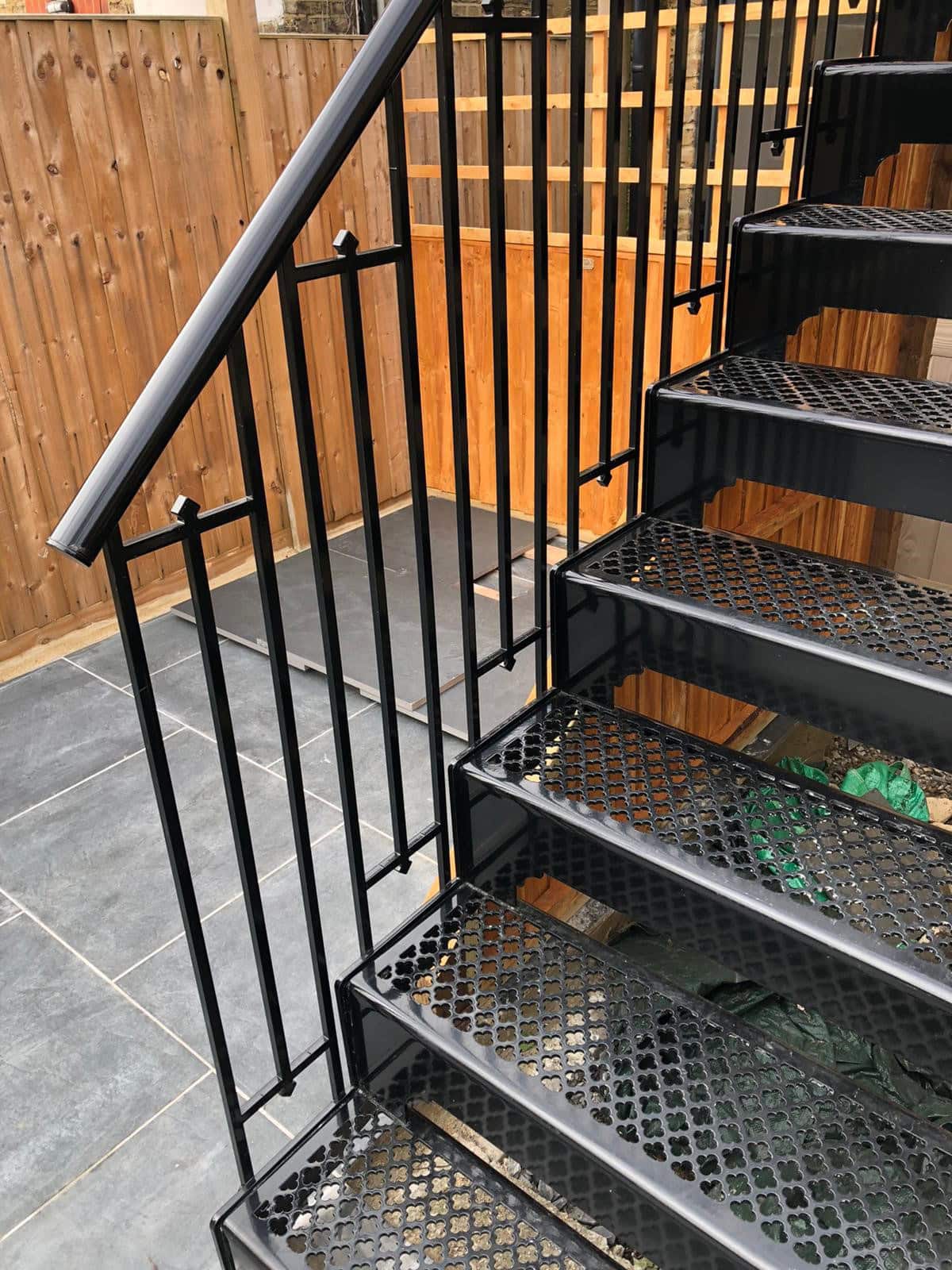 Stainless steel staircase with black railing and wooden fence in an outdoor setting.