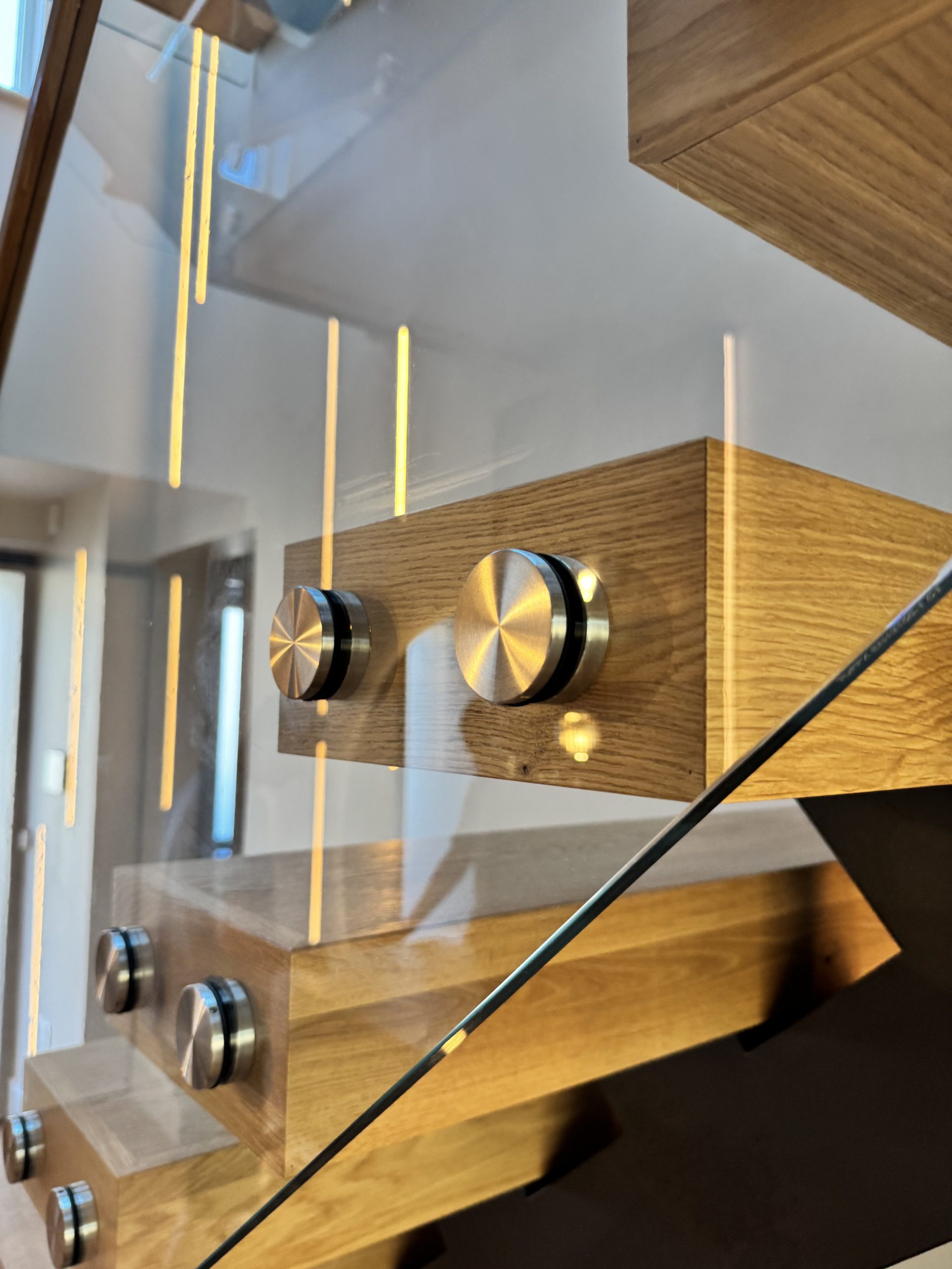 Contemporary wooden staircase with glass balustrade and metal fittings.